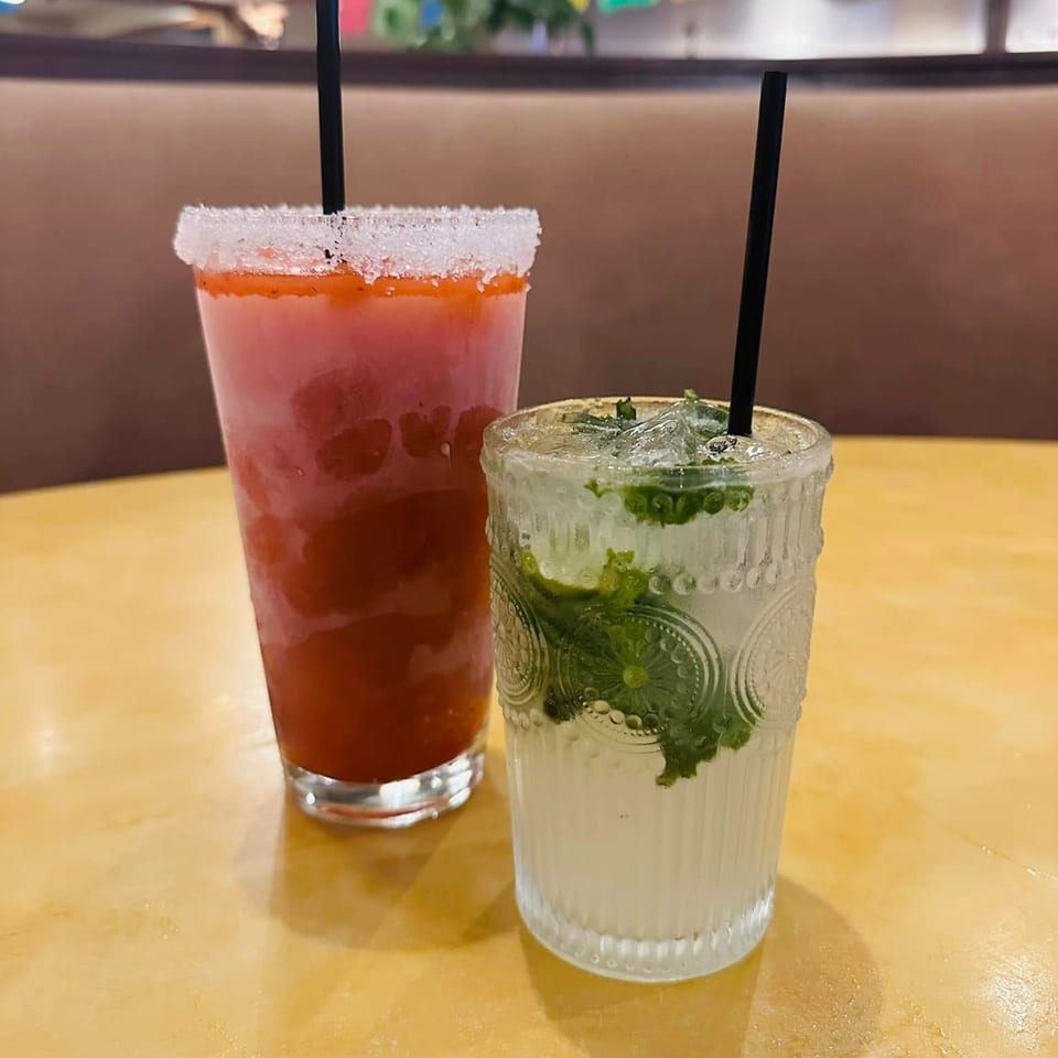 Two refreshing drinks, a red margarita with a salted rim and a mojito, on a yellow table.