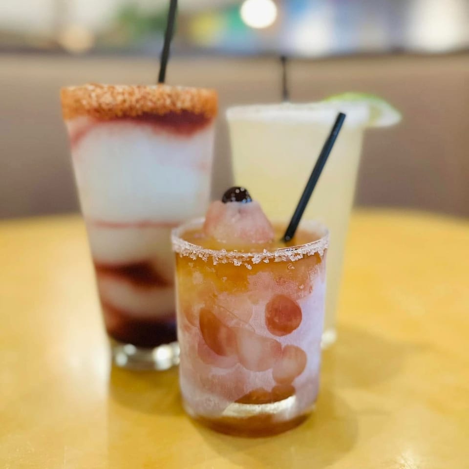 Three colorful, frosty Mexican cocktails, including a margarita, on a yellow table.