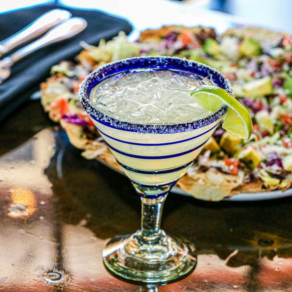 A Fresco's Cocina Mexicana margarita with a lime wedge, next to a plate of nachos.