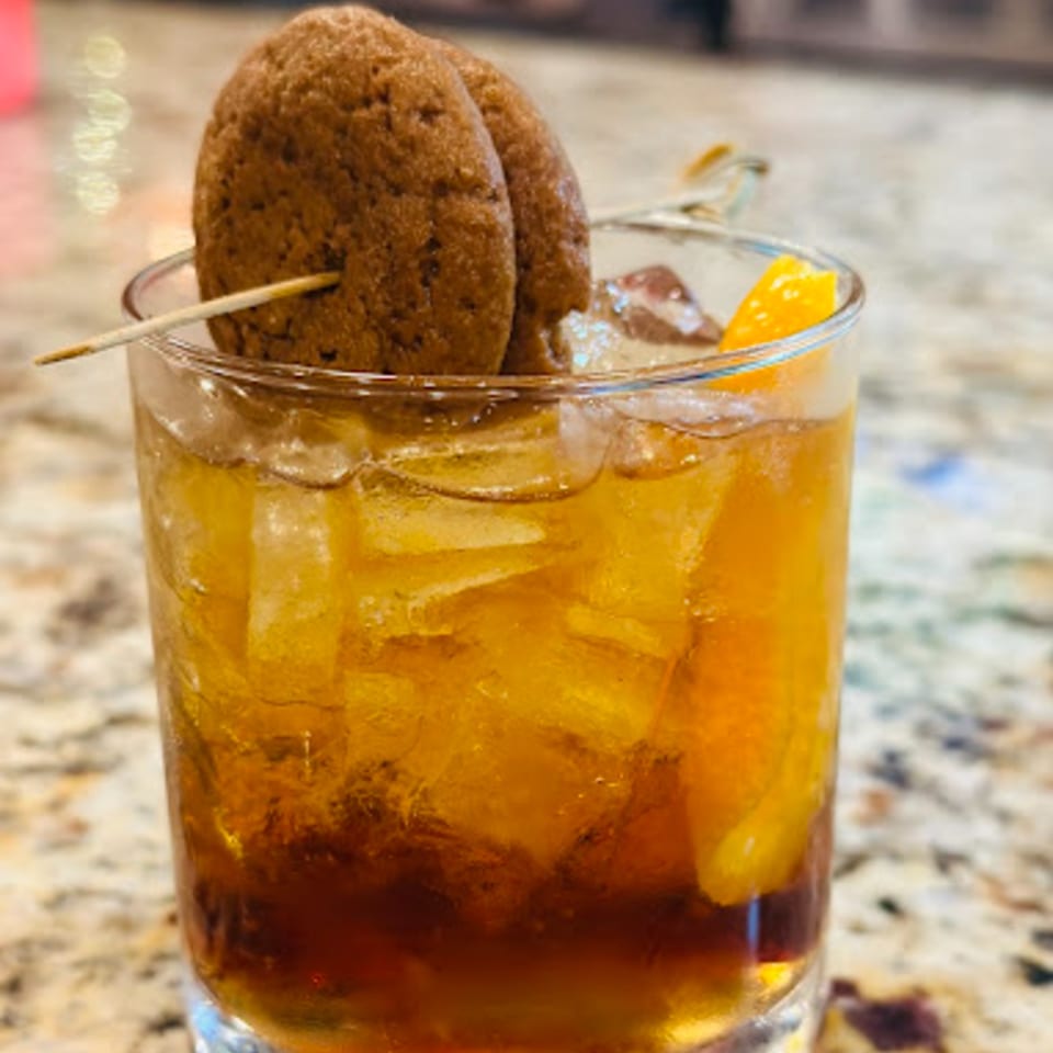 A Fresco's Cocina Mexicana cocktail with ice, orange slices, and two cookies on a skewer.