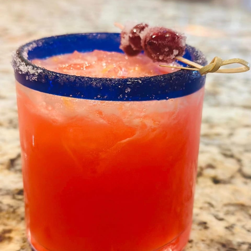 A vibrant red Fresco's Cocina Mexicana margarita in a blue-rimmed glass, garnished with sugared cherries.