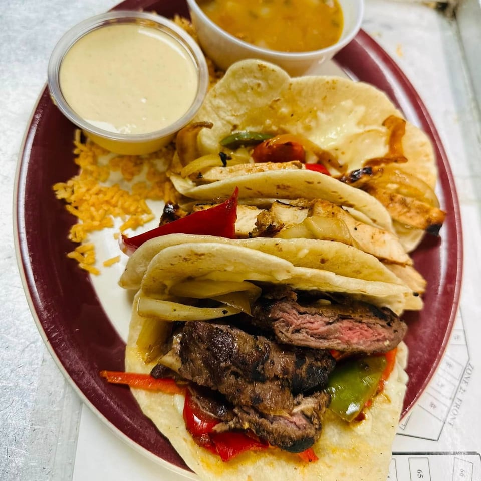 Fresco's Cocina Mexicana fajitas with steak, chicken, peppers, onions, rice, and sauces on a red plate.