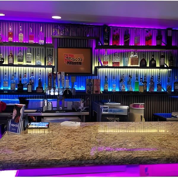 A vibrant bar at Fresco's Cocina Mexicana with purple and blue lighting illuminating liquor bottles.